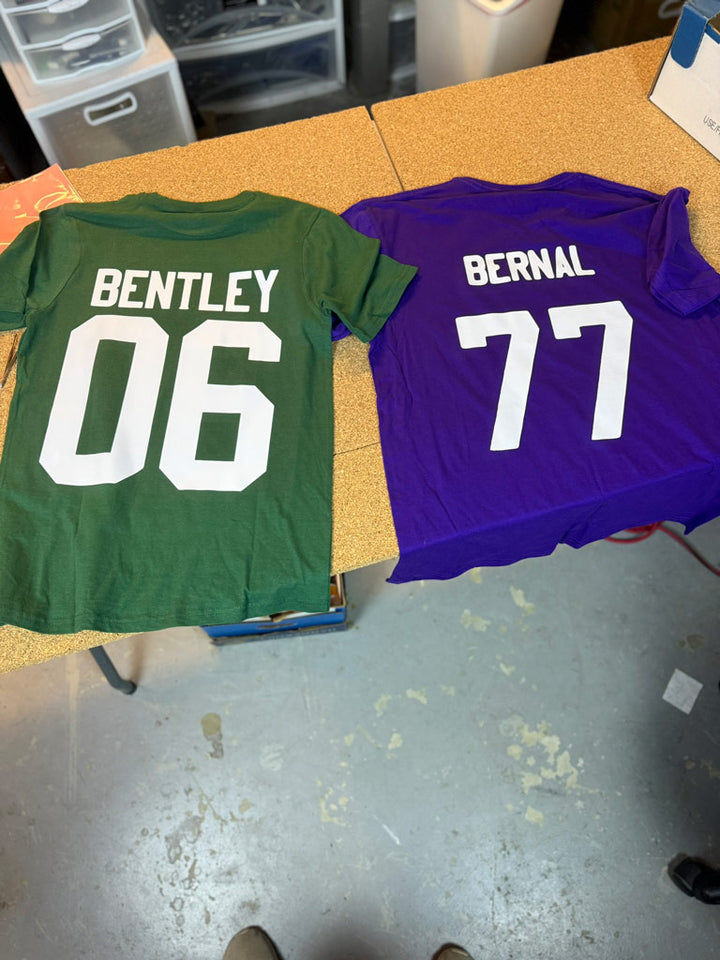 Green and purple custom tees laid flat, printed on backs with “Bentley 06” in white block numbers and “Bernal 77” for personalized team apparel.