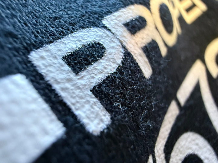 Close-up of white heat-transfer vinyl on black fabric, showing the raised texture and fabric fibers around the printed letter “P.”