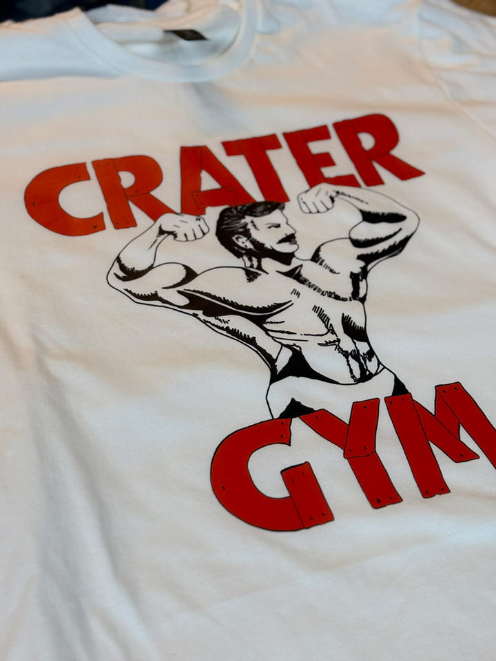 White performance tee printed with bold red “CRATER GYM” text and vintage muscular bodybuilder graphic flexing arms, perfect for fitness branding and gym apparel.