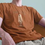 A male model leaning back in a chair wearing a Comfort Colors Tshirt in Yam Orange. The vintage design features a guy in a spooky bedsheet ghost costume standing on a skateboard, with text above him that says Creep It Real.