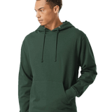 Man in a dark green pullover hoodie with drawstrings and a kangaroo pocket, standing with one hand in pocket