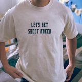 A male model wearing a Comfort Colors Tshirt in Ivory White color with his hands at his sides. There is a funny halloween themed pun on the front of the shirt that says Lets Get Sheet Faced.