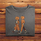 A folded vintage Comfort Colors Tshirt in Pepper Gray color, laying on a wooden table. The retro design features a cute couple walking together on a sidewalk, both wearing matching smiling jack-o-lanterns on their heads. Autumn Fall Vibes.