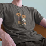 A male model leaning back in a chair wearing a Comfort Colors Tshirt in Pepper Gray color. The vintage design shows two young kids, a boy and a girl wearing fall apparel and pumpkins on their heads, strolling down a sidewalk