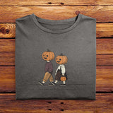 A folded Comfort Colors Tshirt in Pepper Gray color, laying on a wooden table. The vintage design shows two young kids, a boy and a girl wearing fall apparel and pumpkins on their heads, strolling down a sidewalk