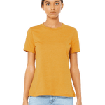 Woman wearing a Bella + Canvas Ladies' Relaxed Jersey Short-Sleeve T-Shirt in the Mustard color, standing with a neutral expression and light blue jeans.