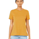 Woman wearing a Bella + Canvas Ladies' Relaxed Jersey Short-Sleeve T-Shirt in the Mustard color, standing with a neutral expression and light blue jeans.