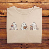 A nicely folded Comfort Colors shirt in Ivory White, laying on a wooden table. The retro design shows three cute little bedsheet ghosts reading books together, in a fun cartoonish art style, giving Fall vibes.