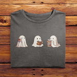 A nicely folded Comfort Colors shirt in Pepper Gray, laying on a wooden table. The retro design shows three cute little bedsheet ghosts reading books together, in a fun cartoonish art style, giving Fall vibes.