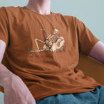 A closeup of a model in a chair wearing a comfort colors Tshirt in Yam Orange color. The vintage includes a relaxed skeleton leaned back on a boulder, smoking a joint. There is text below it that says Built On Strong Joints.