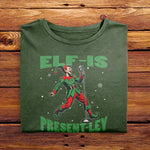 A Moss Green Folded Comfort Colors Tshirt featuring a vintage-style illustration of an elf singing into a microphone. The green text above and below the elf reads ELF-IS PRESENT-LEY, in reference to Elvis Presley, and cute festive snowflakes scattered around.