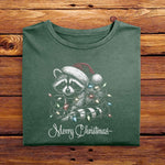 A Moss Green Comfort Colors Tshirt, with a vintage design featuring a cute raccoon wearing a Santa hat, wrapped in colorful Christmas lights. Merry Christmas is written below in a playful script font, perfect for holiday cheer.