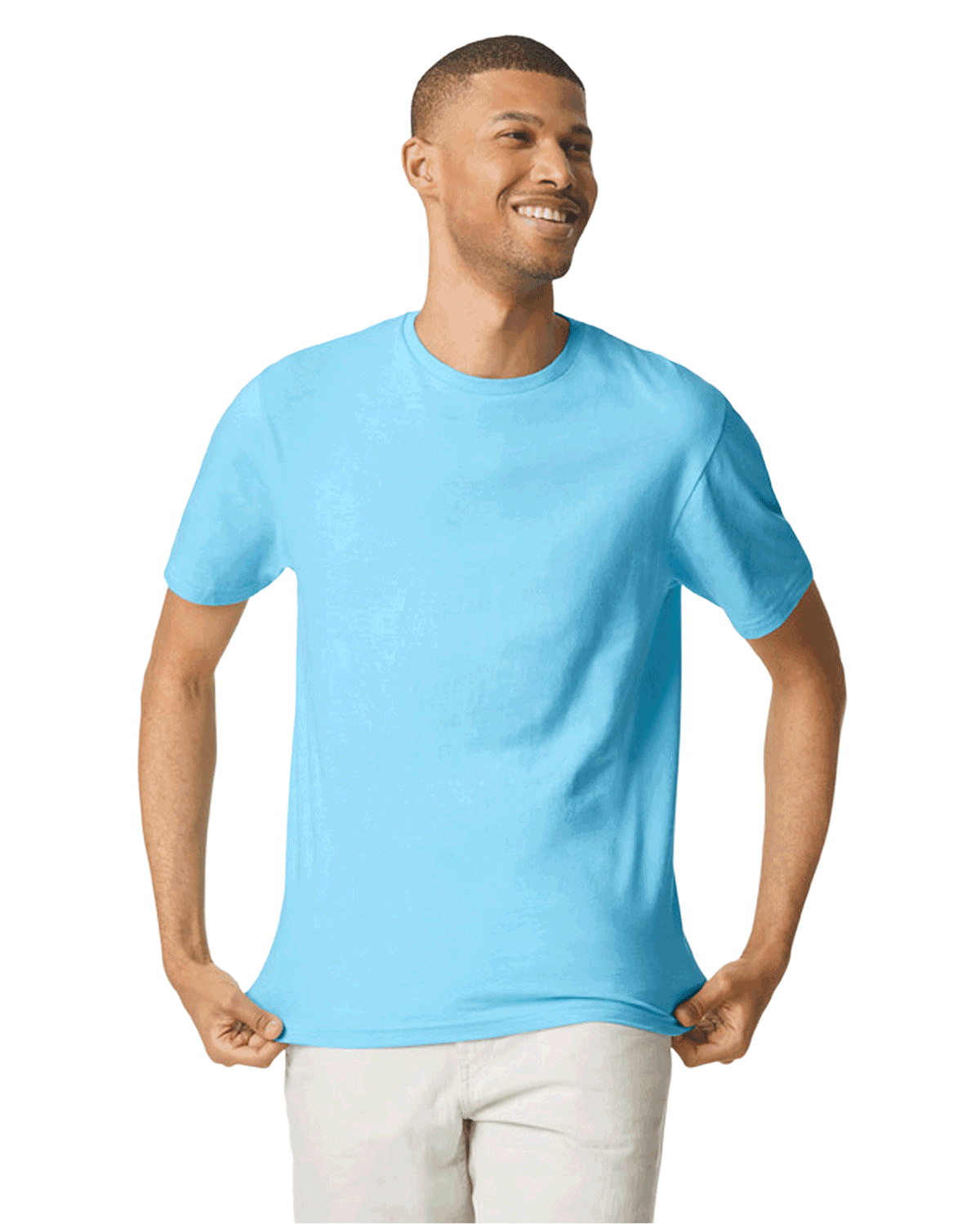 Man wearing a Gildan SoftStyle T-shirt in "Sky" color, standing with a relaxed posture and smiling while holding the hem of his shirt.