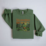 A vintage green sweatshirt with a retro graphic print of a spooky town with a large pumpkin in front of a building. The text on the sweatshirt reads Halloweentown Est. 1998