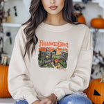 A brunette female model wearing a vintage tan sweatshirt with a retro graphic print of a spooky town with a large pumpkin in front of a building. The text on the sweatshirt reads Halloweentown Est. 1998