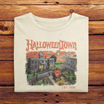 A vintage Comfort Colors Tshirt in Ivory White with a retro graphic print of a spooky town with a large pumpkin in front of a building. The text on the sweatshirt reads Halloweentown Est. 1998