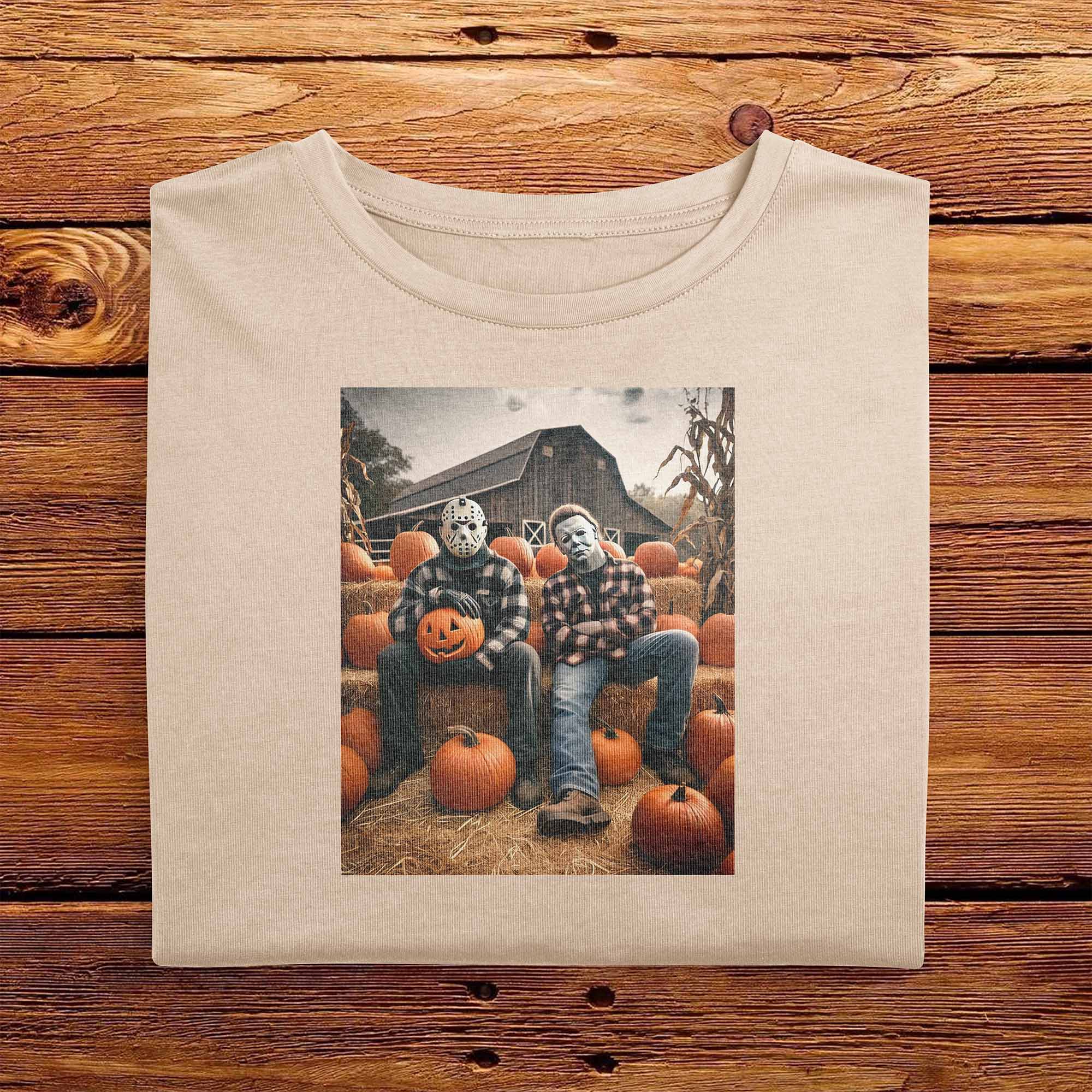 An Ivory White folded Comfort Colors Tshirt, laying on a wooden table. The vintage design has Jason Vorhees from Friday the 13th, and Michael Meyers from Halloween, both in cozy flannels sitting together in a pumpkin patch. Jason is showing off his jack o lantern