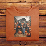 A Yam Orange folded Comfort Colors Tshirt, laying on a wooden table. The vintage design has Jason Vorhees from Friday the 13th, and Michael Meyers from Halloween, both in cozy flannels sitting together in a pumpkin patch. Jason is showing off his jack o lantern