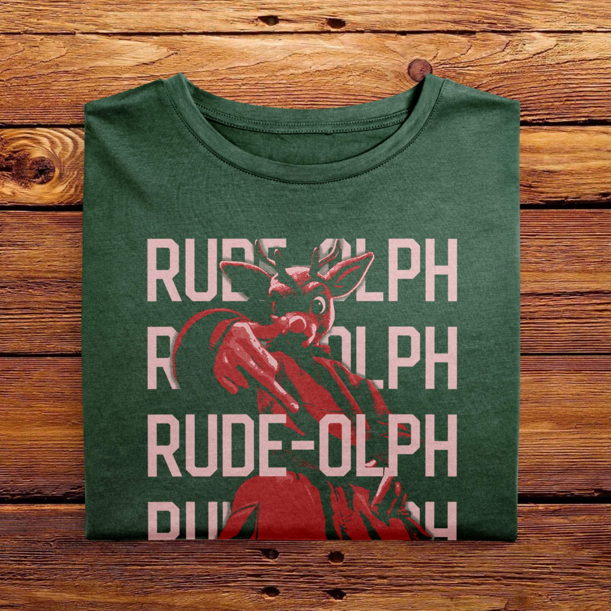 A vintage folded Moss Green comfort colors shirt. The retro design features Rudolph the Red Nosed Reindeer in a y2k merch artstyle, posed in a rude manner. There is text that says Rude-olph, a funny festive pun with his name to go with the graphic