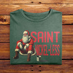 A Folded Comfort Colors Moss Green Sweatshirt featuring a vintage design. The design features Santa Clause sitting down seemingly on the sidewalk, appearing to be struggling financially. The text beside him reads Saint Nickel-Less, poking fun at his misfortune