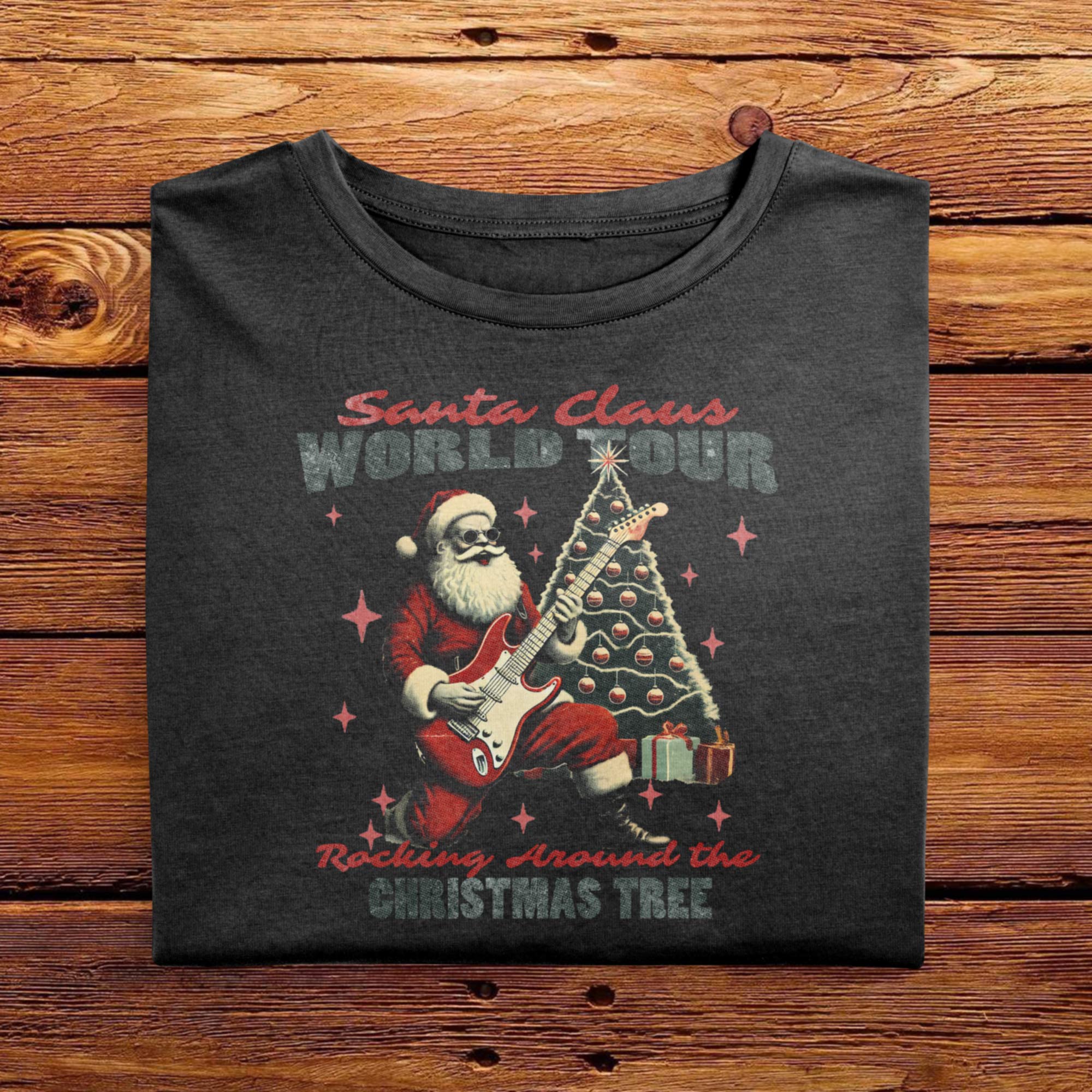 A laid out Black Comfort Colors Tshirt. The design features a vintage illustration of Santa Claus shredding the guitar, with a christmas tree behind him. The drawing is joined with the words Santa Claus World Tour, Rocking Around The Christmas Tree