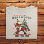 A laid out Ivory White Comfort Colors Tshirt. The design features a vintage illustration of Santa Claus shredding the guitar, with a christmas tree behind him. The drawing is joined with the words Santa Claus World Tour, Rocking Around The Christmas Tree