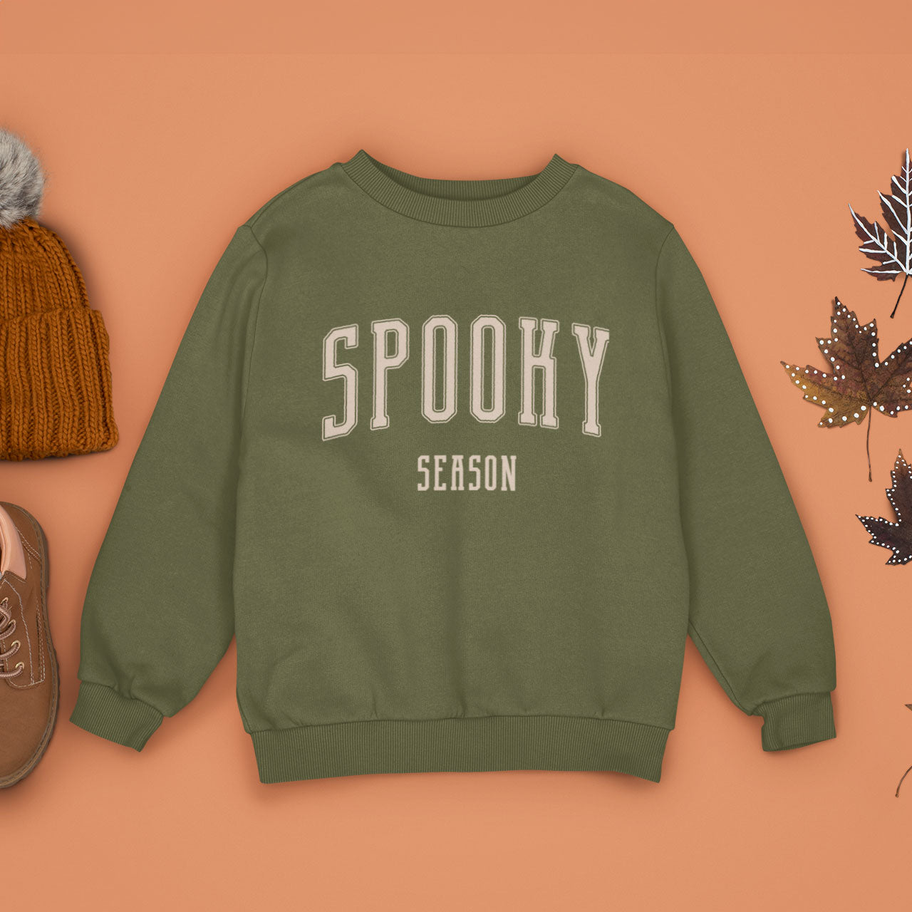 A Fresh Olive Green Crewneck Champion Power blend Sweatshirt, on an earthy autumn backdrop. This design features the words: Spooky Season, in an off white scholarly university font.