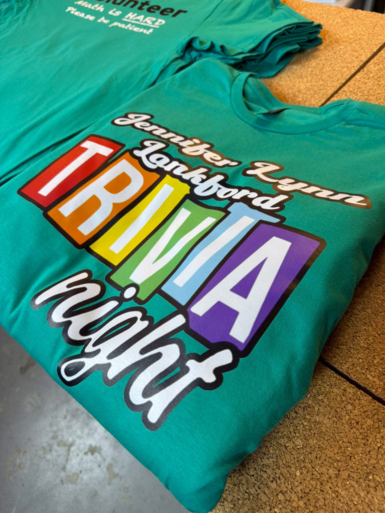 Green custom t-shirt printed with “Jennifer Lynn Lankford TRIVIA night” in rainbow block letters and cursive script for event apparel.