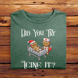 A Moss Green Comfort Colors Tshirt featuring a playful design of a gingerbread nurse and injured gingerbread man in a hospital bed. The text reads Did You Try Icing It? Perfect holiday gift for nurses, bakers, or those with a sense of humor.