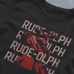 A video of a laid out black comfort colors shirt. The retro design features Rudolph the Red Nosed Reindeer in a y2k merch artstyle, posed in a rude manner. There is text that says Rude-olph, a funny festive pun with his name to go with the graphic